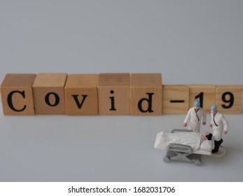 The Printed COVID-19 Disease Blocks Are Made From Wood Being On White Background. The Concept Is That Miniature Of Doctors Who Are Taking Care Of The Patient Who Develops These Infectious Disease.