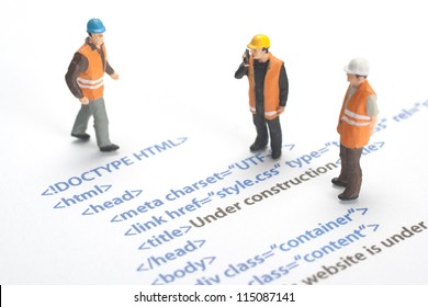 Printed HTML code of website (internet page) under construction. Construction worker figurines working on code.