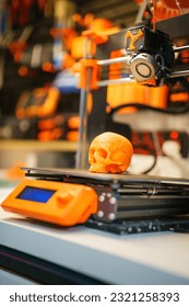 Printed human skull. 3d printer head. Card from below. Spool with filament in the background. Creating prototypes. Orange plastic. Prototype printing. Hobby and study.