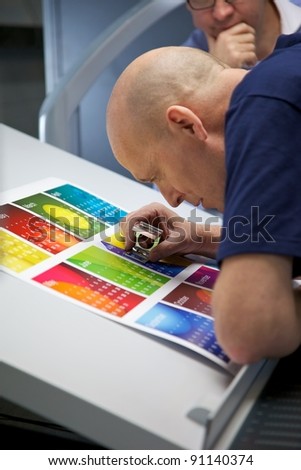 Printer looking through an eye glass to check the registration on a printed calendar