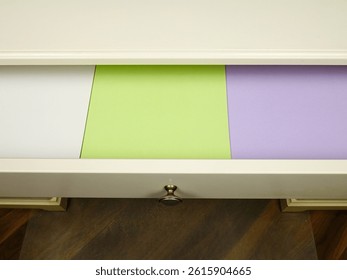 Printer papers of different colors are in a desk drawer