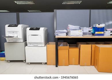 Printers, business documents stack on desk and cardboard boxes under desk.