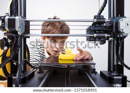 Printing on 3D printer figurines of toys from white plastic close-up. Boy happily and emotionally takes the finished printed figure from the working platform of the printer and goes into the play