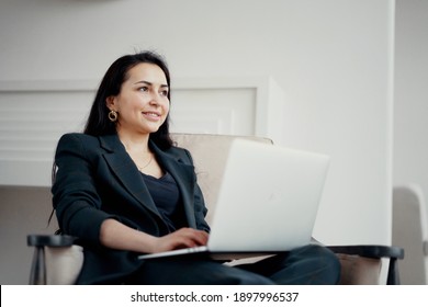 prints text on a laptop. a brunette businesswoman sits in a chair and smiles. Good mood great go up things on the project at work. Stylish, bright, modern office in the city center. - Shutterstock ID 1897996537