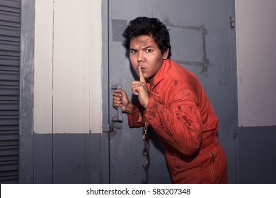 Prison Breaker In Orange Jump Suit Making Silence Gesture While Trying To Open Metal Door, Shhh!!