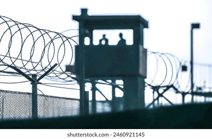 prison environment, watchtower with guards on duty, spiraled razor wire barriers ensuring containment and safety, cells incarceration law enforcement walls criminal justice system punishment