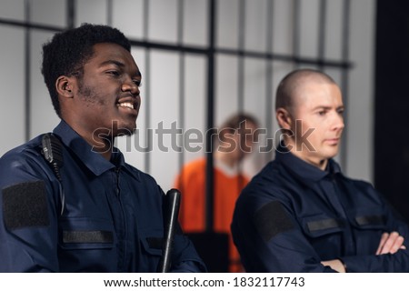 Prison guards smile as they stand with batons near cells with dangerous criminals. Multi-racial portrait
