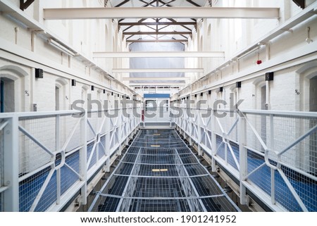 Prison landing beams row of cells block victorian British English jail house with bed in room lock up high security room derelict old new category A B C in custody with bars open confined escaping
