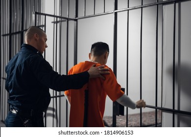 The prison warden puts the prisoner behind bars after the court verdict and locks the cell - Shutterstock ID 1814906153