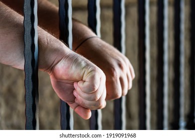 Prisoner Man Holding Hands On Jail Bars. Hands On Prison Bars.