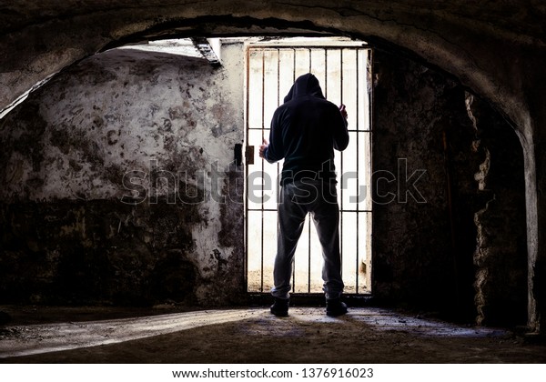 囚人は古い地下室に立って閉じこもり バーの背後からシルエット 暗い地下室の中で必死の孤立感を持つ囚人 人権拒否のコンセプト の写真素材 今すぐ編集