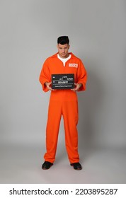 Prisoner In Orange Jumpsuit With Mugshot Letter Board On Grey Background