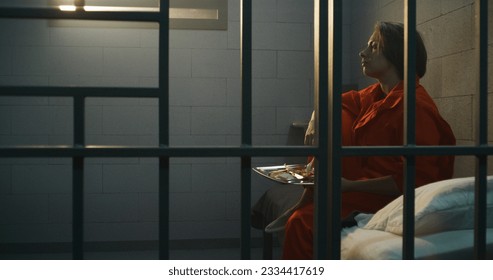 El prisionero con uniforme naranja ofrece la cena de comida sirviendo tranvía a una criminal en prisión. La mujer criminal sentada en la cama, cumple condena de prisión por delito en la cárcel o centro de detención.