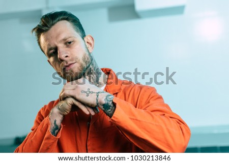 prisoner with tattoos looking at camera in prison cell