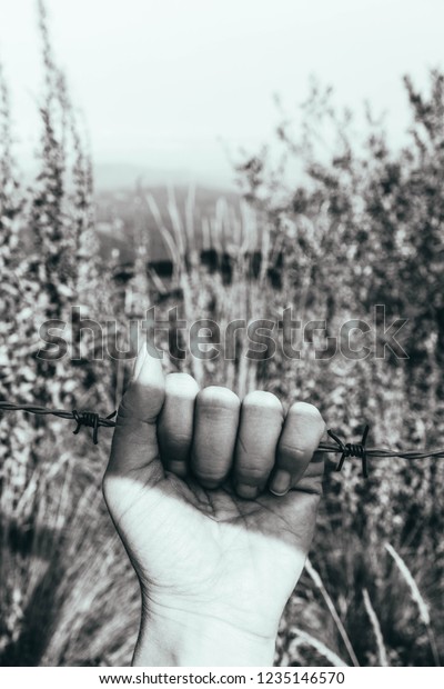 Prisoners hand,\
holding a barbed wire fence. Restricted area, freedom struggle,\
jail prison terror,\
jailbreak.