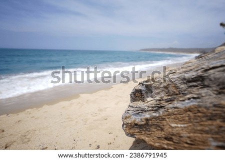 Pristine Baja California (lower California region of Mexico) pacific beach from creative angle with large slanted boulder and bright blue ocean waves and white sand