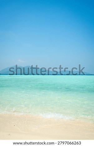 A pristine beach scene showcasing soft golden sand meeting crystal-clear turquoise waters. The horizon features lush green mountains, creating a tranquil and inviting tropical escape. Perfect for travel, tourism, and vacation marketing. Ideal for beach resort promotions, travel brochures, and relaxation-themed content. Sunlit and vibrant, this image captures the essence