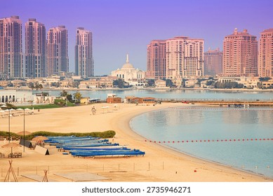 Pristine beach shoreline in Doha extending along the water, with modern high rise buildings and mosque architecture dominating the cityscape