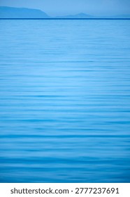 Pristine blue water surface spanning across the vertical frame towards a barely visible landmass in the distance.