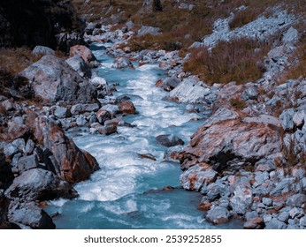 Pristine mountain stream flowing through rugged terrain, surrounded by rocks and natural vegetation. The clear, turquoise water contrasts beautifully with the earthy tones of the rocky landscape. - Powered by Shutterstock