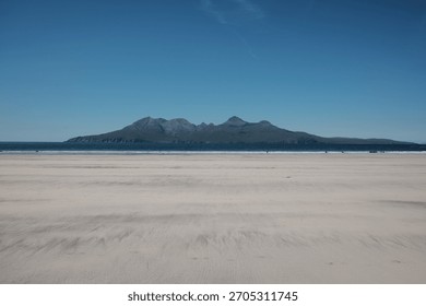 Pristine sandy beach with mountain range in the distance under a clear blue sky