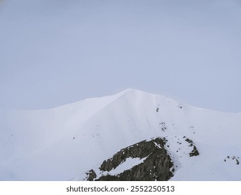 A pristine snowy mountain peak rises against a clear blue sky. The smooth slopes and untouched snow create a serene and majestic alpine landscape. - Powered by Shutterstock