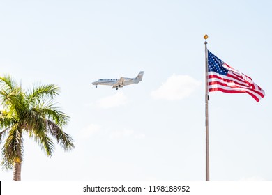 Private charter plane flying isolated in sky with american flag closeup, tropical palm tree in Naples, Florida