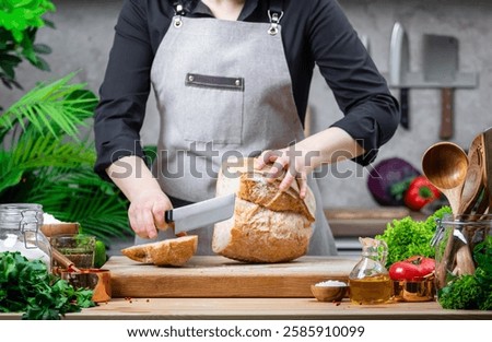 Private chef cutting white bread on cozy kitchen with wooden table, kitchenware and ingredients for cooking. Homemade baking, cooking, food blogging
