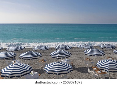 Private clubs with blue and white sun parasols along the turquoise sea in the French Riviera at the Promenade des Anglais. - Powered by Shutterstock