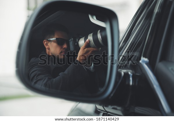 Private detective with camera spying from auto,\
view through car side\
mirror
