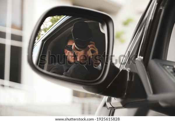 Private detective with camera spying from auto,\
view through car side\
mirror