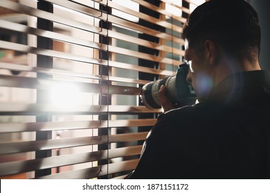 Private detective with camera spying near window indoors - Powered by Shutterstock