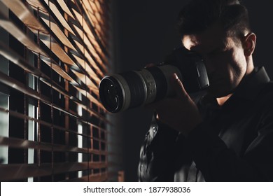 Private detective with camera spying near window indoors - Powered by Shutterstock