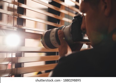 Private detective with camera spying near window indoors - Powered by Shutterstock