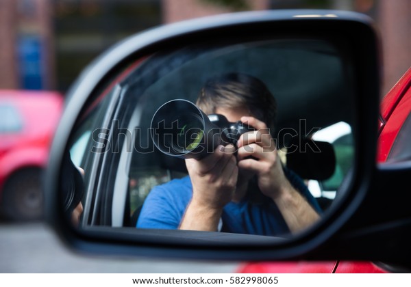 Private Detective Sitting In Car Photographing\
Reflected In Wing\
Mirror