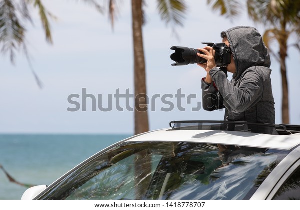 Private detective spying with camera looking through\
sunroof  of a car.