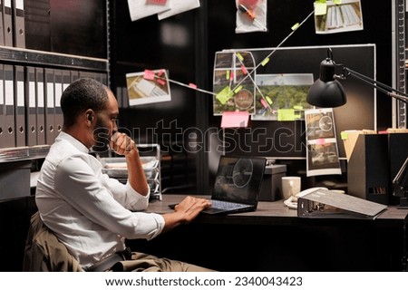 Private detective wathing cctv camera photos on laptop while sitting at workplace desk. African american investigator analyzing surveillance photographs on computer screen
