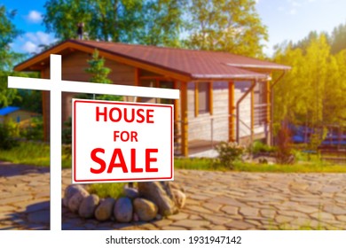 Private House For Sale. House For Sale Sign On The Background Of A Blurry Image Of A Cottage. Buying And Selling Real Estate. Rural Properties. Sale Of Houses In Rural Areas.