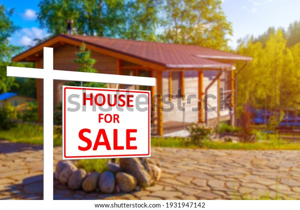 Private house\
for sale. House for sale sign on the background of a blurry image\
of a cottage. Buying and selling real estate. Rural properties.\
Sale of houses in rural\
areas.