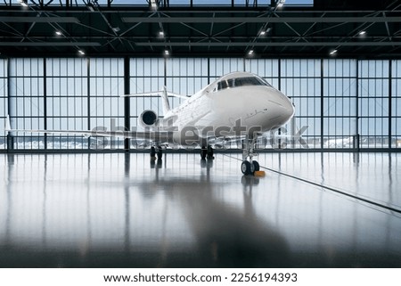 Private jet airplane at the huge white hangar waiting for maintenance and repair jobs. Expensive and luxury trip is waiting after a passengers. Business jet prepared for departure. Luxury life
