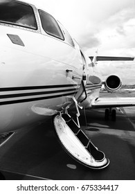 Private Jet Sitting On The Tarmac With Its Door Open Urging You To Come Aboard. Also Captures The Jet Engine And The Wing Of The Airplane. Black And White Edition.