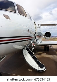 Private Jet Sitting On The Tarmac With Its Door Open Urging You To Come Aboard. Also Captures The Jet Engine And The Wing Of The Airplane.