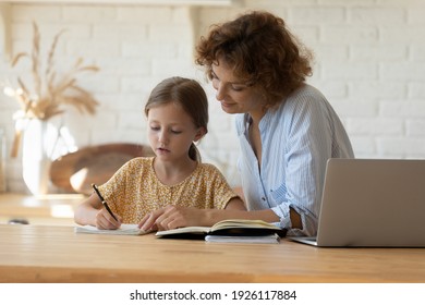 Private Lesson. Attentive Young Woman Tutor Teacher Help Little Girl Pupil With Studying Math Language Correct Mistakes Explain Learning Material. Smiling Mother Assist Small Daughter With Home Task