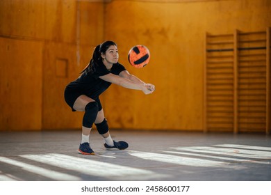 Pro female volleyball player in action passing a ball with a bump while playing a match in a sports hall. Portrait of a woman playing volleyball during a training on an indoor court. Copy space. - Powered by Shutterstock