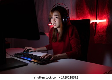 Pro player gamer young asian woman playing online video game shooting fps tournament ranking cyber internet at night red neon light room with gaming headset and keyboard on championship event.