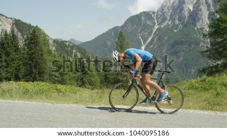 Pro road cyclist enduring a difficult mountain ascent on his cool bicycle. Determined Caucasian sportsman looks down and grits his teeth as he ascends a challenging mountain in the hot summer sun.