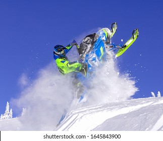 A Pro Snowmobiler Makes A Jump With A Big Blast Of Snow And Epic Falls. Background Of Blue Sky Leaving A Trail Of Splashes Of White Snow. Bright Snow Bike And Suit. Snowmobile