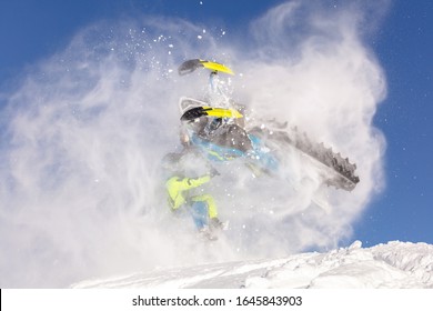 A Pro Snowmobiler Makes A Jump With A Big Blast Of Snow And Epic Falls. Background Of Blue Sky Leaving A Trail Of Splashes Of White Snow. Bright Snow Bike And Suit. Snowmobile