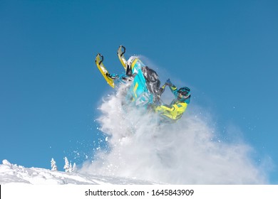 A Pro Snowmobiler Makes A Jump With A Big Blast Of Snow And Epic Falls. Background Of Blue Sky Leaving A Trail Of Splashes Of White Snow. Bright Snow Bike And Suit. Snowmobile