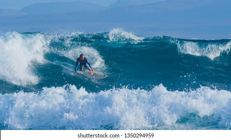 Pro Surfer Dude Surfing Fun Ocean Waves In Sunny Canary Islands. Cheerful Male Surfboarder Looking Around Sunny Canary Islands While Carving A Clear Blue Wave. Athletic Man Having Fun On Surfboard